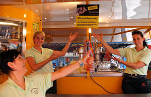Das Foto zeigt 3 Kellnerinnen an einem Tresen, die auf das Plakat &quot;Wir machen mit&quot; weisen.