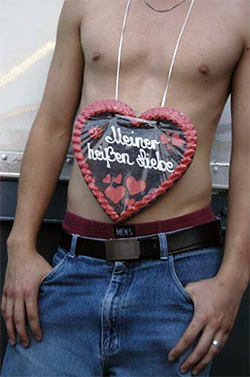 Foto des Torsos eines jungen Mannes, der ein Lebkuchenherz mit der Aufschrift &quot;Meiner heißen Liebe&quot; um den Hals trägt.